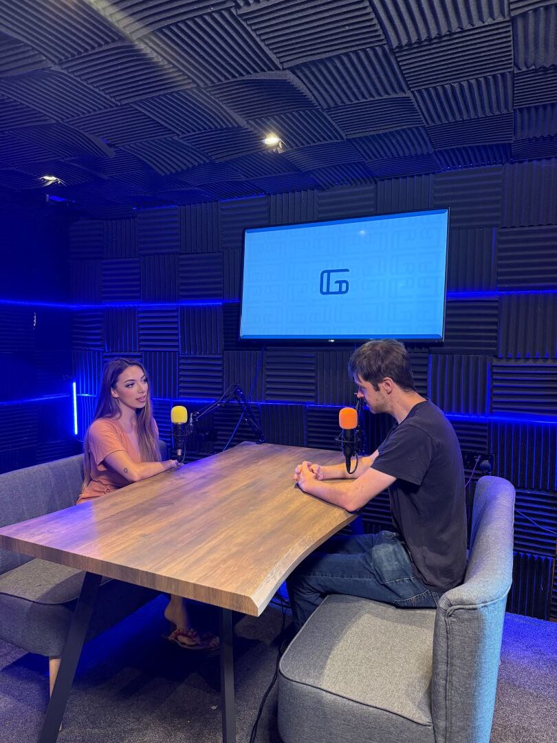Man and woman chatting into mic in the podcast studio