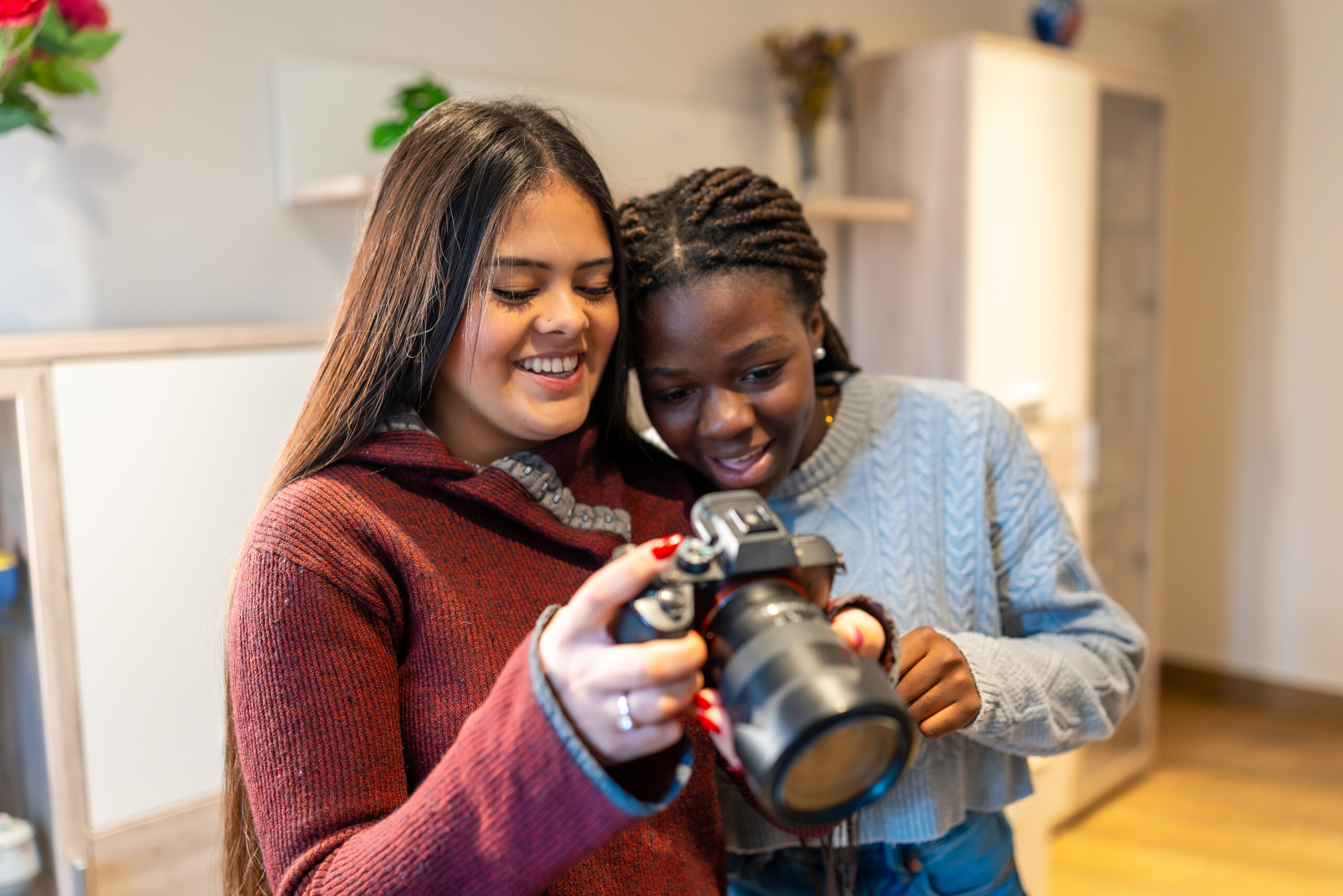 Two smiling female students reviewing photos on dslr camera at home Two girls viewing their work on the camera